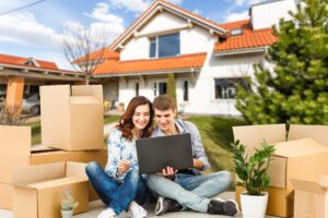 Jeune couple devant une maison neuve entourés de leurs cartons symbole de l'accession à la propriété grâce au PTZ 2026